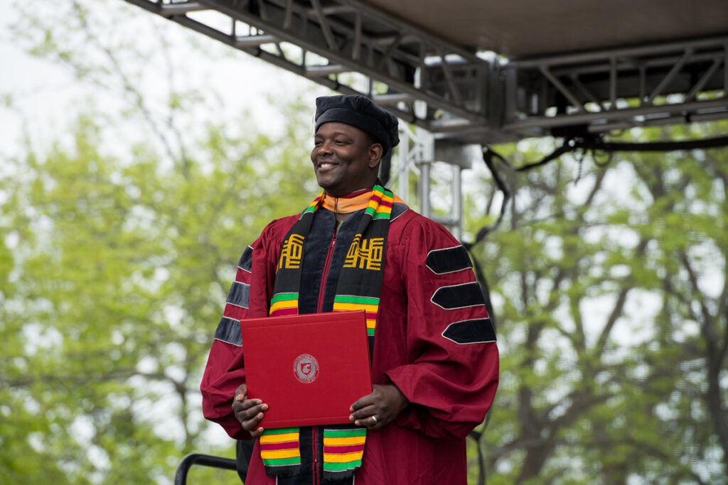 Abel Saba smiles as he holds a WSU diploma during an outdoor commencement ceremony.