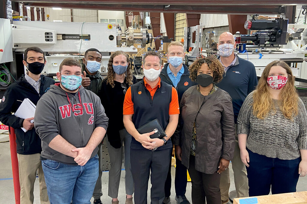 Washington State University and Clemson University students pose together inside a manufacturing facility.