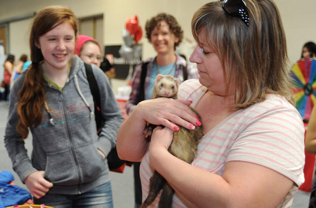 A woman holds a ferret while others watch.