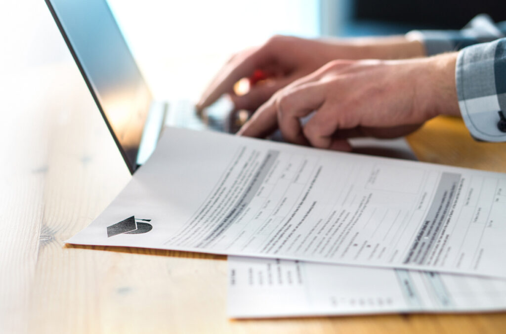 A man types on a computer while looking at an admissions application