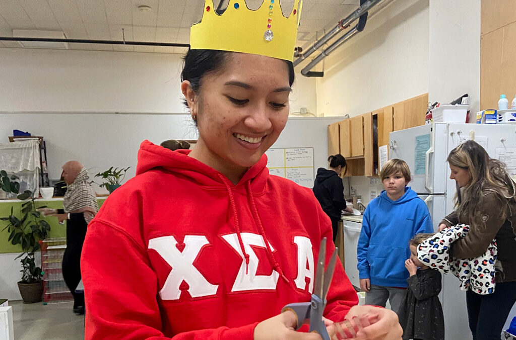 A sorority member wearing Greek letters cutting items to decorate paper crowns.