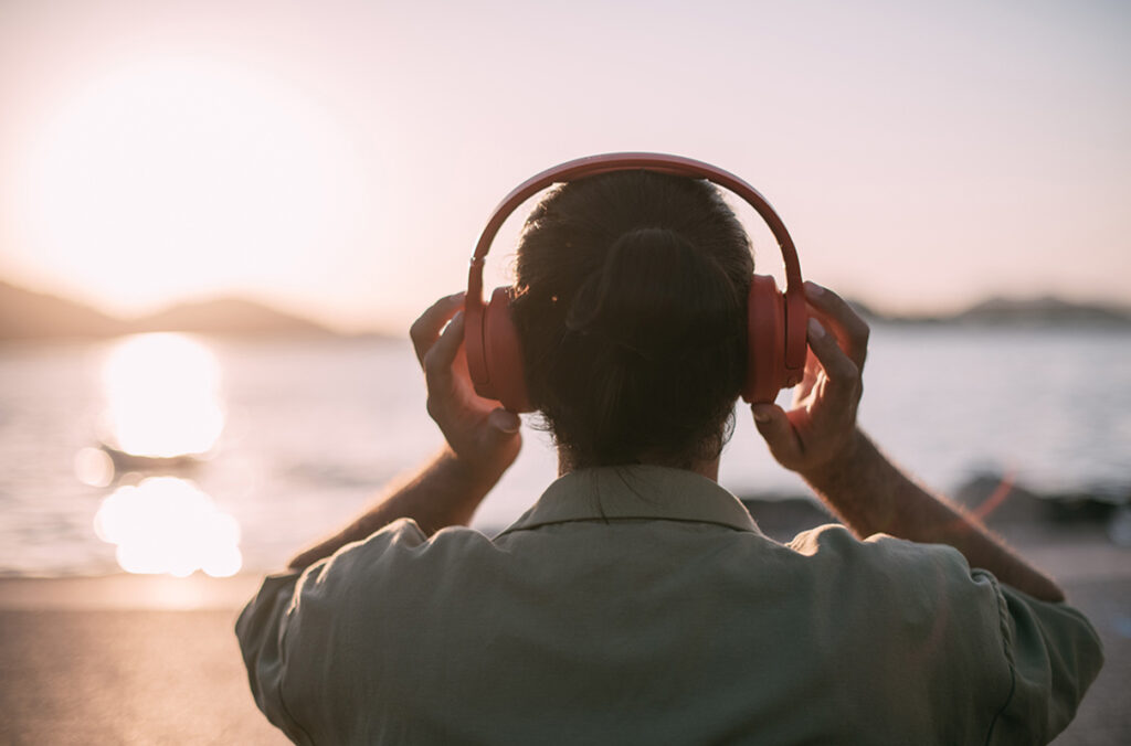 A person listens to headphones while looking at the ocean.