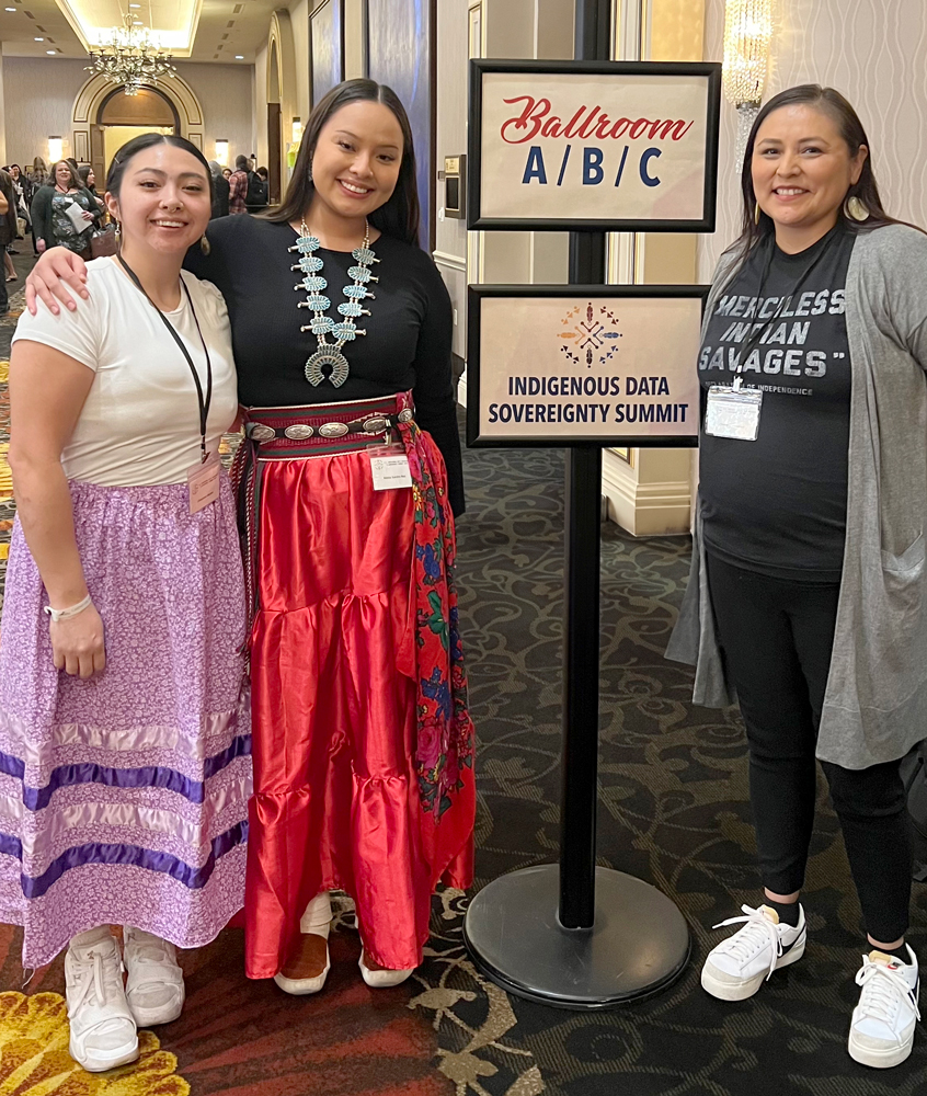 Cheryl Ellenwood and two WSU students standing next to a sign at the Indigenous Data Sovereignty Summit.