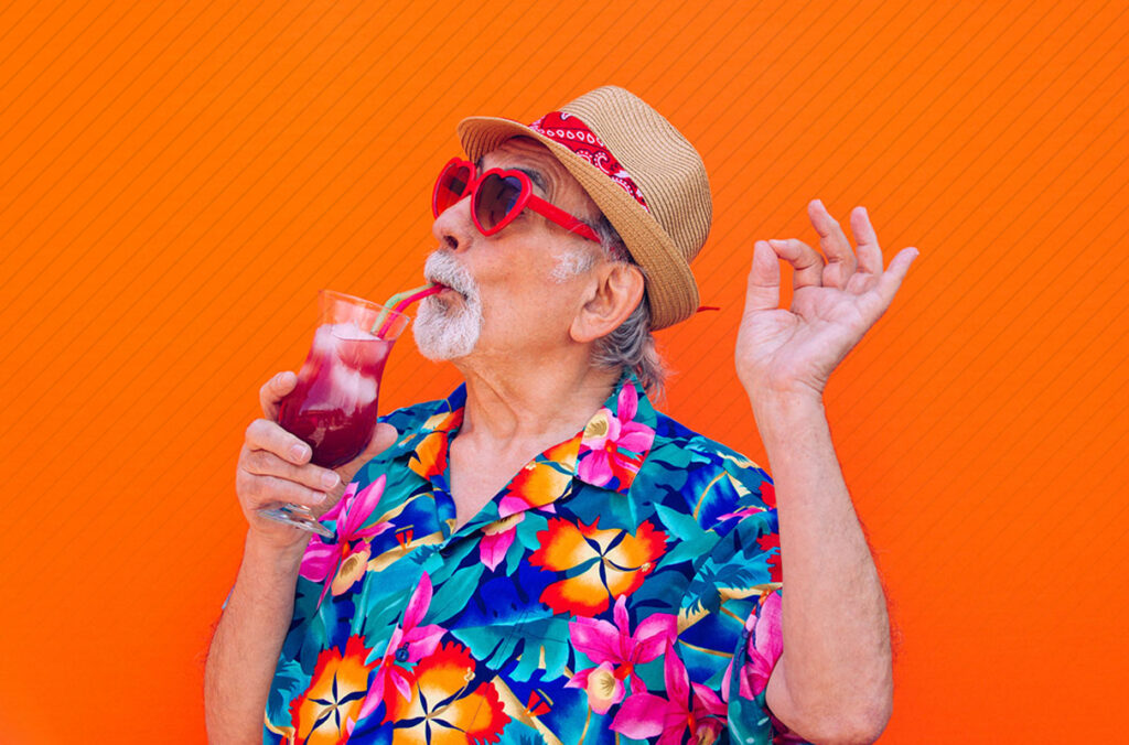 A man with a white goatee wearing a Hawaiian shirt and sipping a tropical drink.