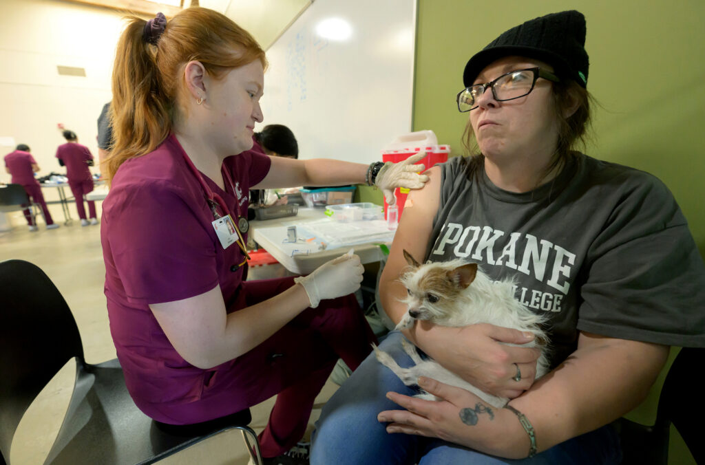 Amy Fain receives a vaccination while holding her dog, Hercules.