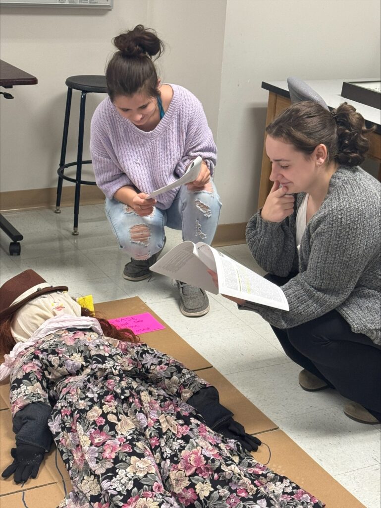 WSU students Jazminn Kalmakoff, left, Madalyn Munafo examine the recently deceased Elinor Rickardsen as they analyze the forensic entomological evidence of Rickardsen’s murder for a class project.