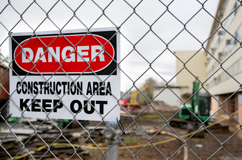 A danger sign on the fence of a construction site asking people to keep out.