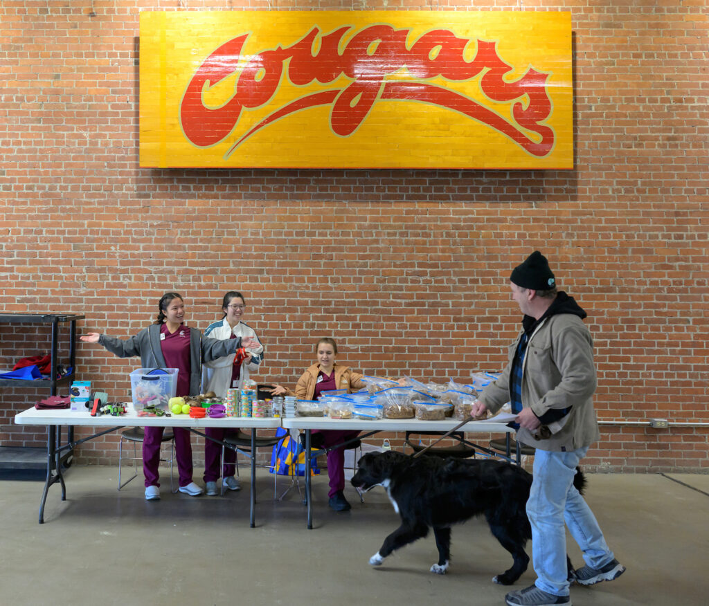 Three nursing students offering free pet products to a dog and its owner.