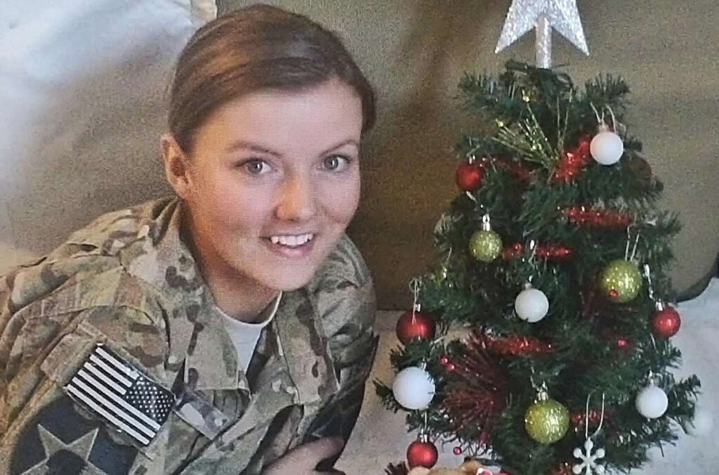 Closeup of Ashley Aday in military uniform next to a small Christmas tree.