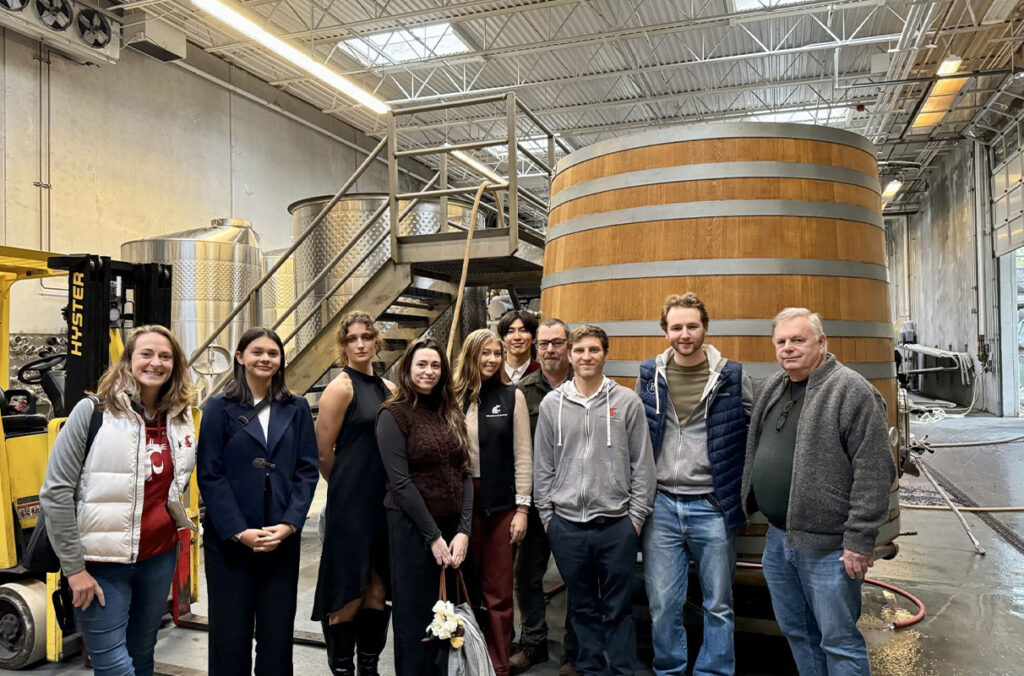 WSU students posing for a group photo while touring the production space of a winery.