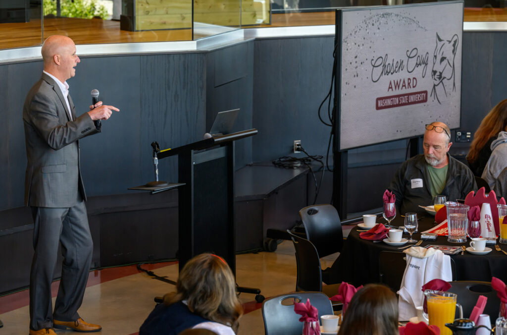 Dave Cillay speaking to a crowd seated at tables during an awards ceremony.
