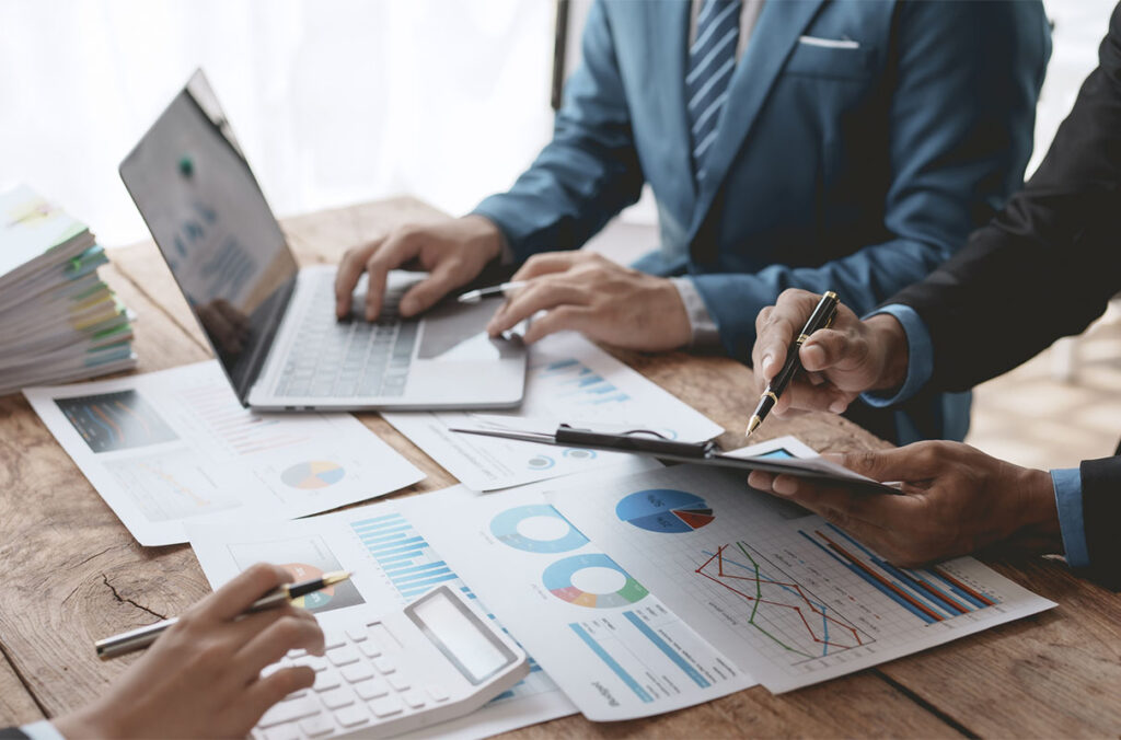 Closeup of three business people analyzing data with a laptop computer and printouts of multiple charts.