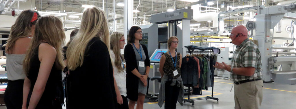 Students gather near a Cotton Inc. employee in a production factory.
