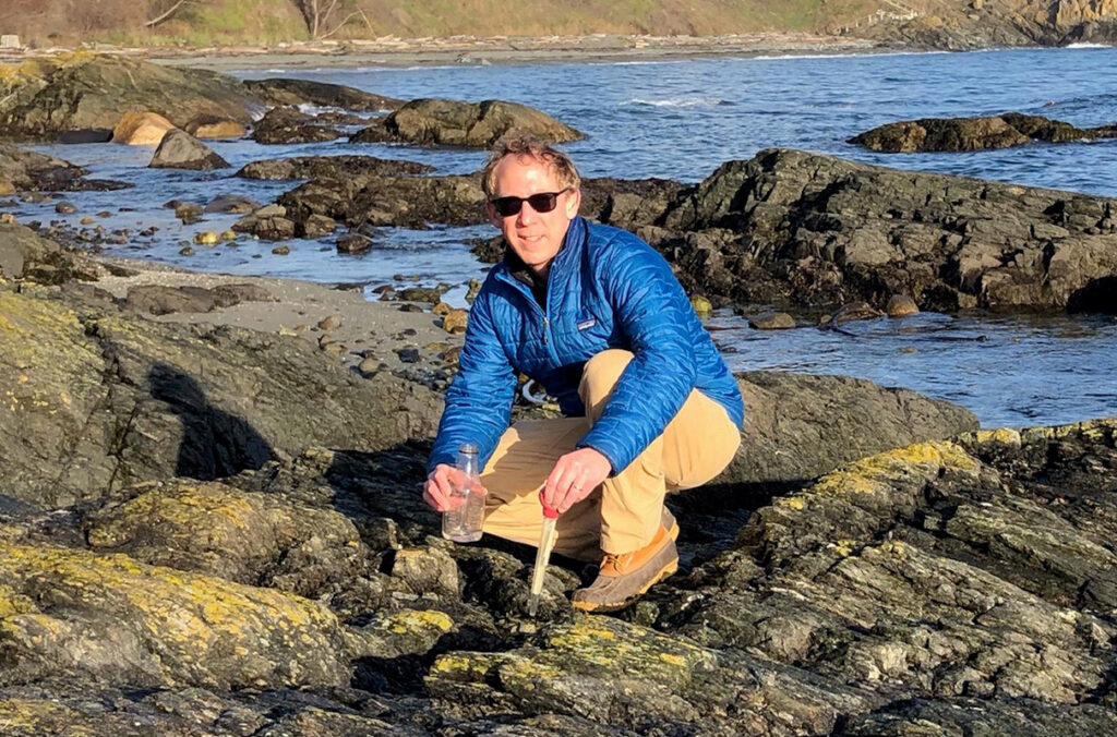 Wes Dowd crouching on a rocky shore to collect samples.