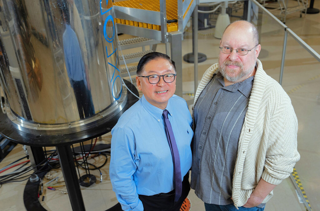 Two men standing next to a nuclear magnetic resonance instrument.