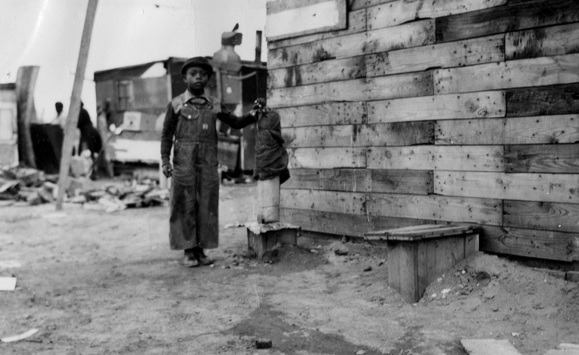 Black and white photo of a child standing next to a community water tap in Pasco, Washington.