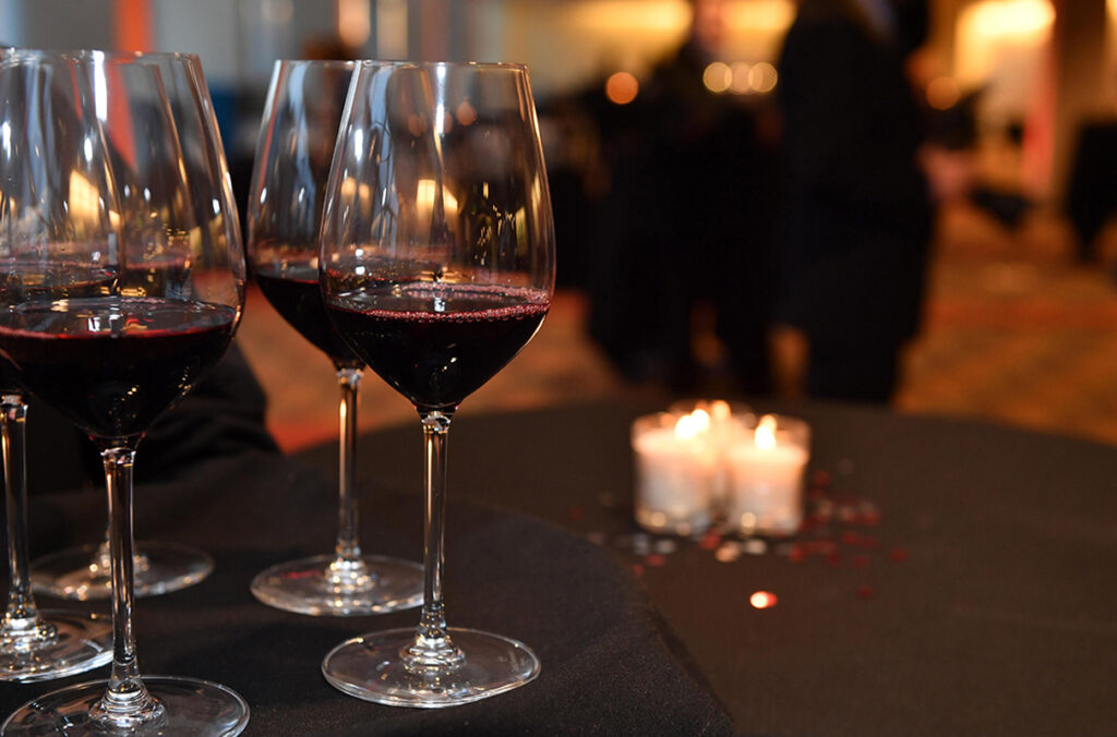 Closeup of five glasses of red wine on a candle-lit table.