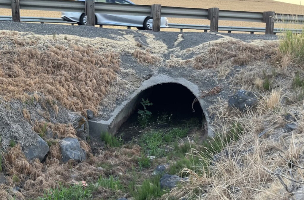 A culvert under a roadway as a car travels over it.