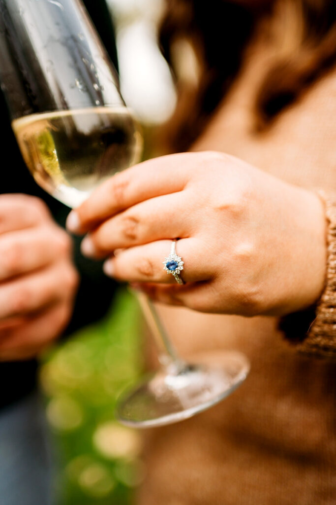 Closeup of an engagement ring as someone holds a glass of champagne.