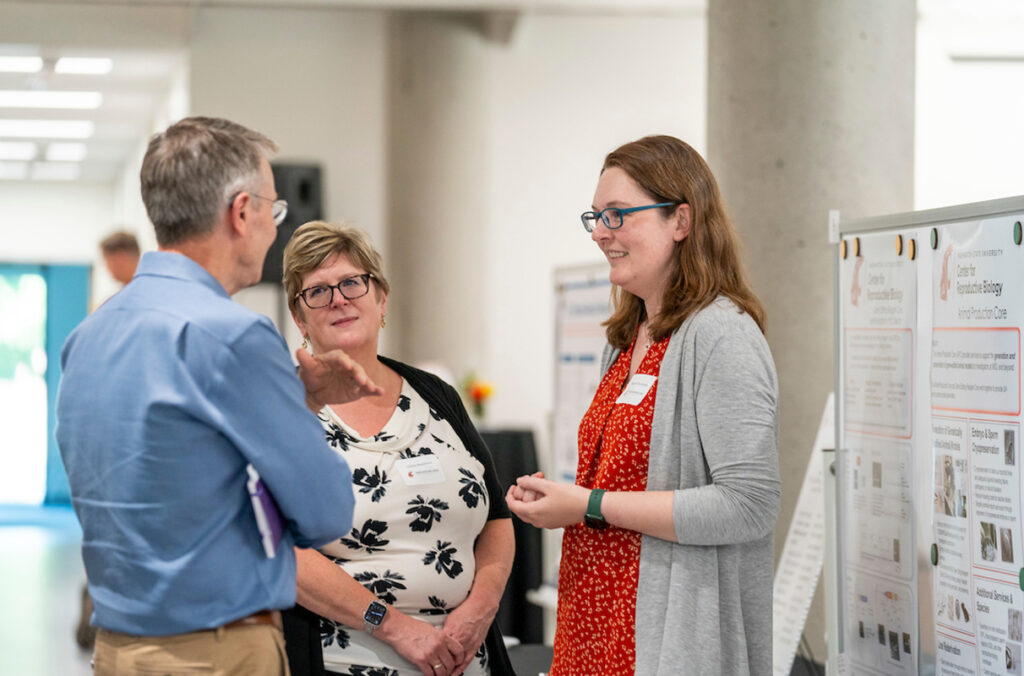 Three people standing and talking in front of a research poster display.