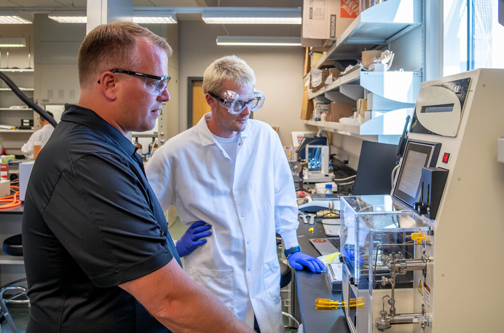 Two researchers standing in front of a piece of complex research equipment looking at a computer screen.