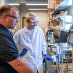 Two researchers standing in front of a piece of complex research equipment looking at a computer screen.