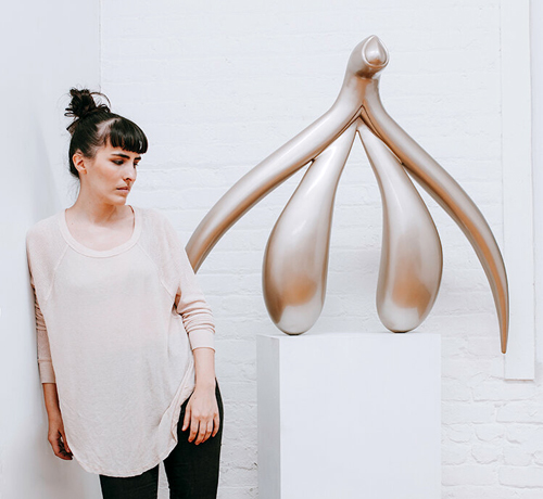 Sophia Wallace leaning against a wall next to a piece of artwork on a pedestal.