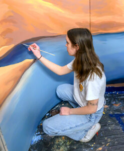Andrea Zimmerman kneeling and painting a mural.