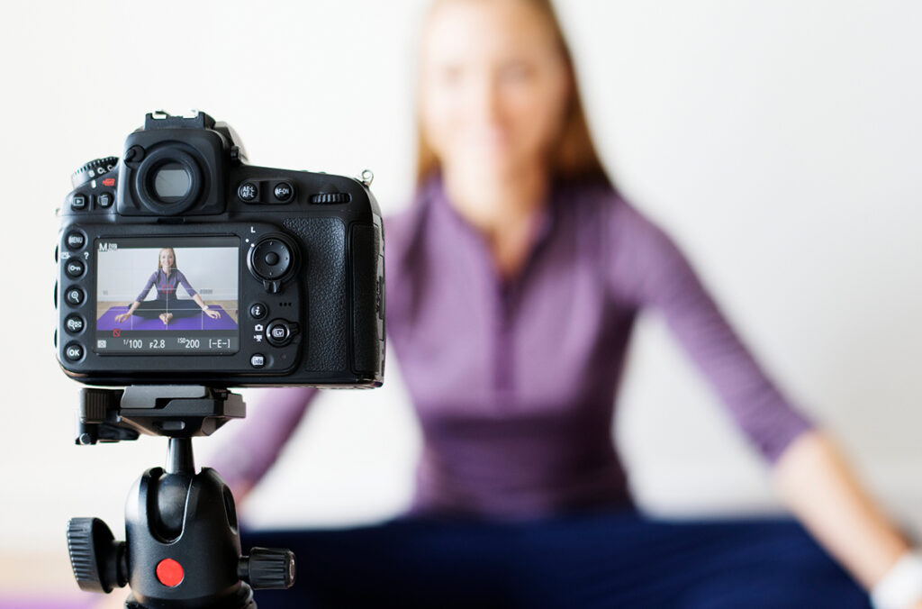 A fitness influencer recording herself on a camera while doing yoga.