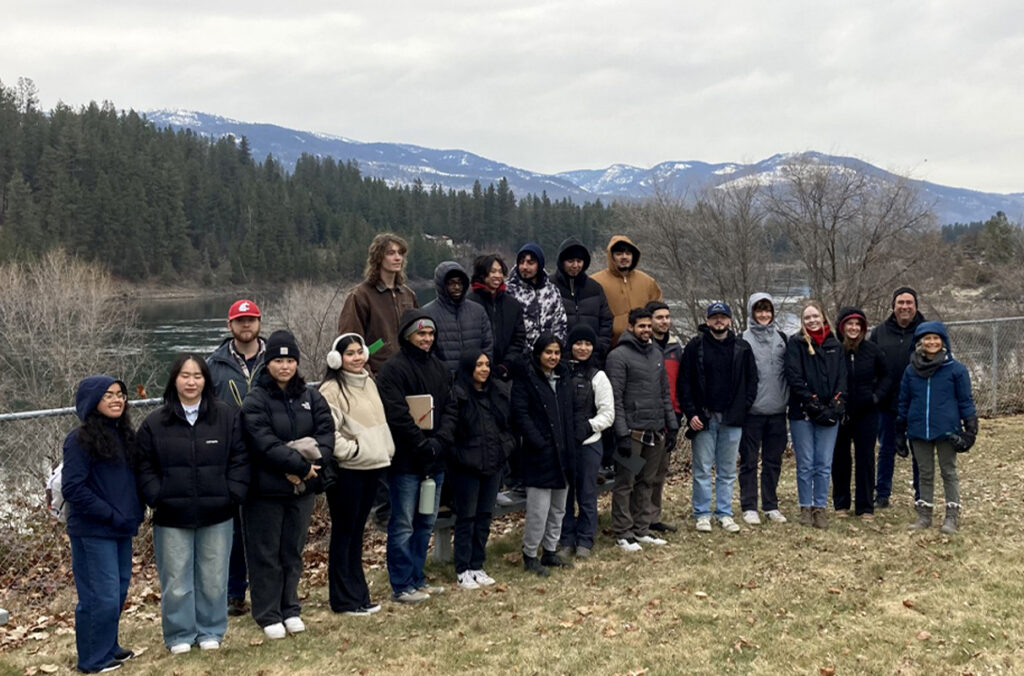 A group photo of students and faculty in front of a fence along the Northport waterfront.