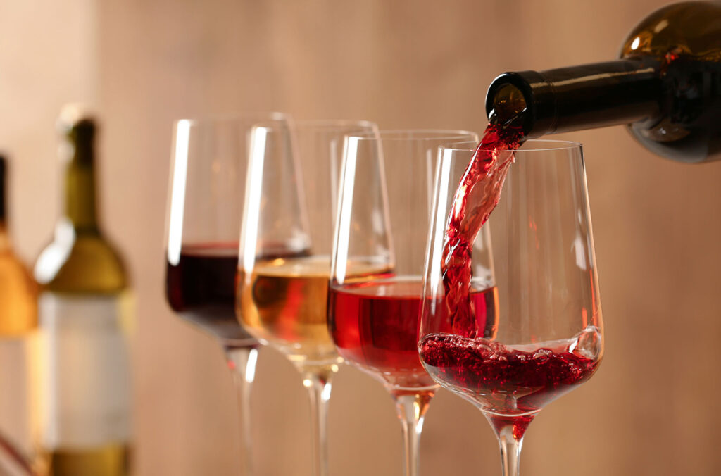 A closeup of three glasses of wine as a bottle finishes pouring into a fourth.