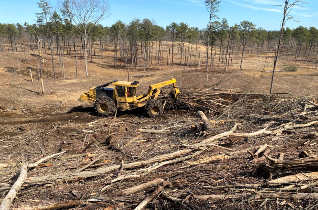 A large tractor removing a pile of trees and debris.