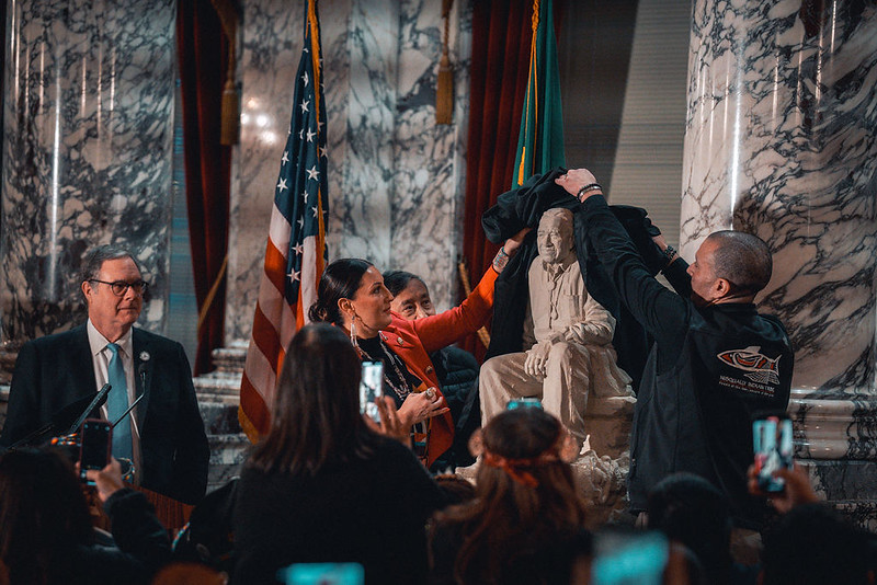 Two people unveil a maquette of a statue design in front of a crowd.