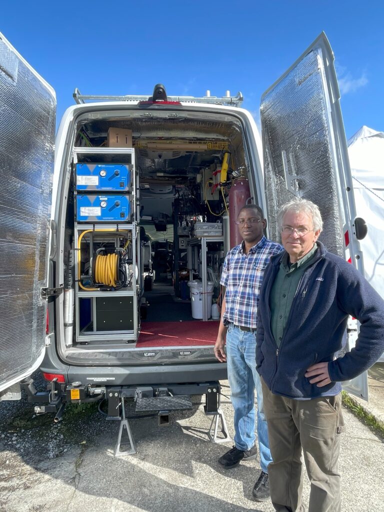 Tom Jobson, professor in the Department of Civil and Environmental Engineering, and postdoctoral researcher Adeniyi Olufemi Adesina stand in front of a van loaded with equipment.
