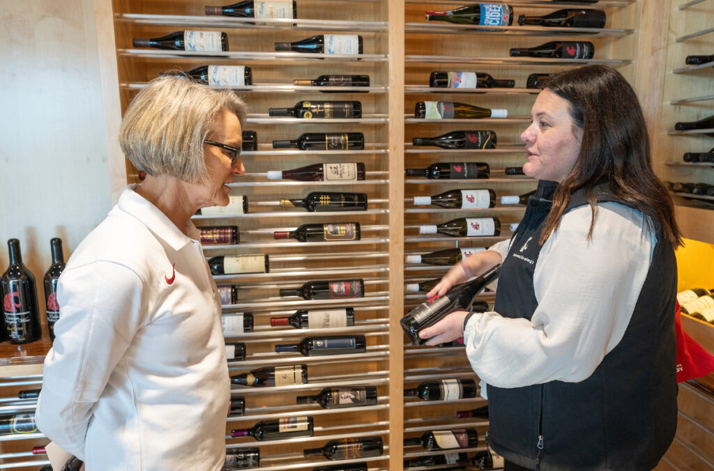 WSU President Elizabeth Cantwell speaking to someone in front of racks filled with bottles of wine.