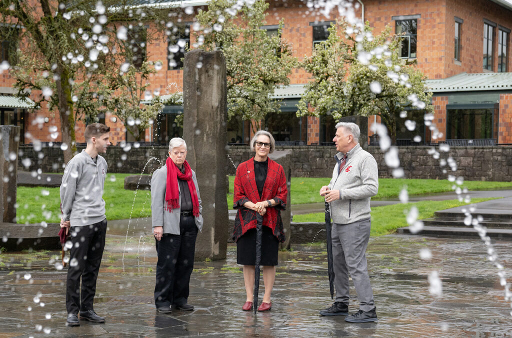 WSU President Elizabeth Cantwell posing for a photo with others as a fountain shoots water overhead.