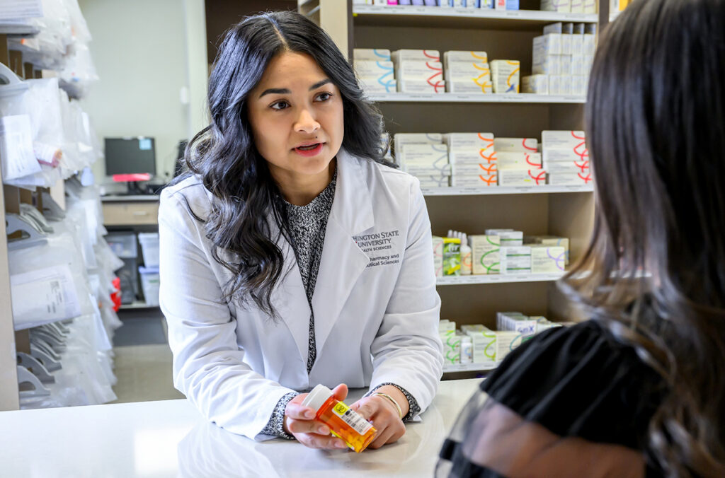 Catalina Yepez holding a prescription bottle while consulting a pharmacy patient.