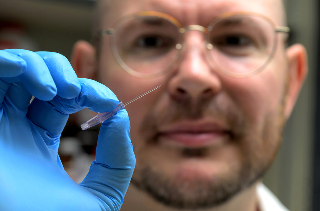 A closeup of Arden Baylink and his gloved hand holding a thin glass tube.