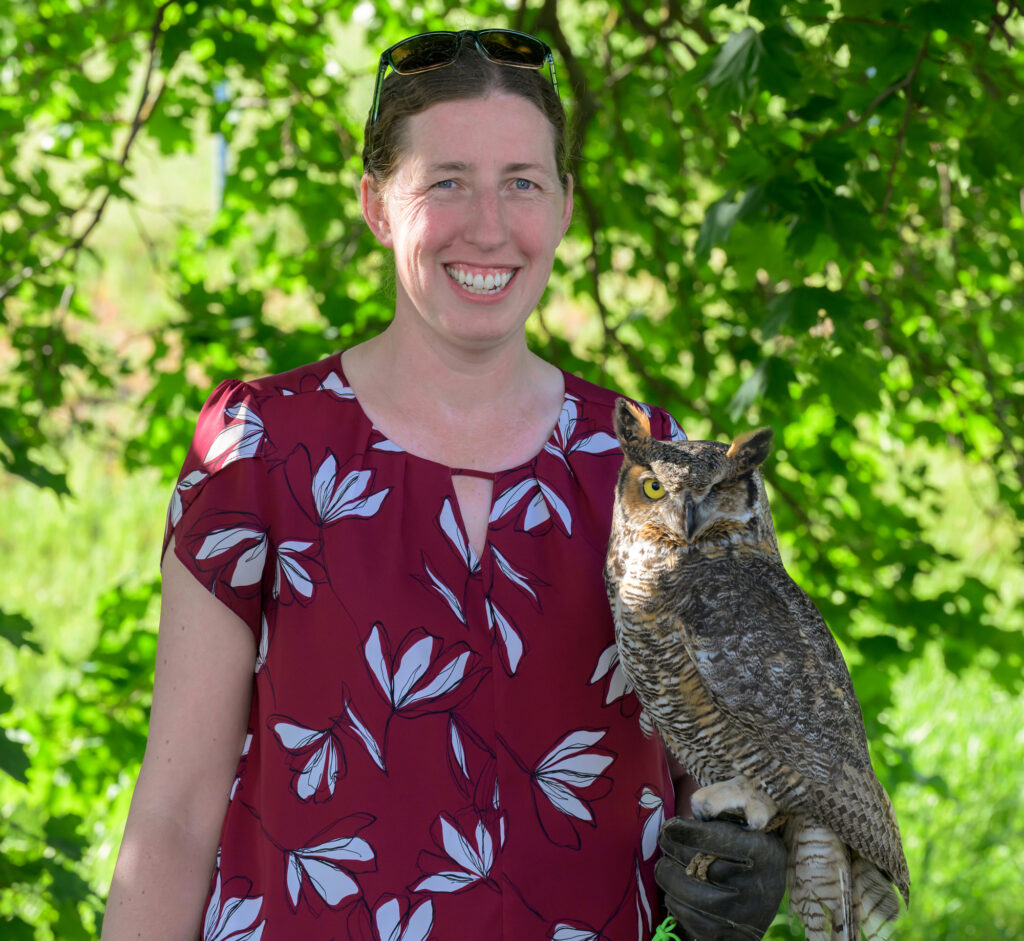Dr. Marcie Logsdon posing with Eugene the owl in front of a tree.