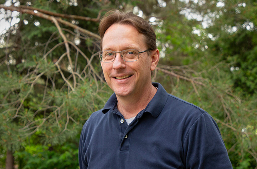 Closeup of Ian Burke standing in front of several trees.
