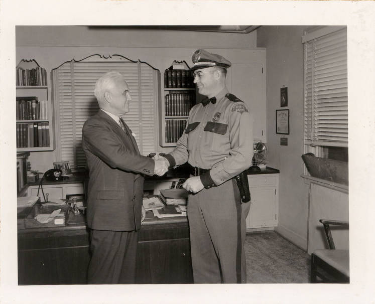 A July 1950 photo of Lt. Charles Kinzel of the Washington State Patrol shaking hands with Washington State College President Wilson Compton.
