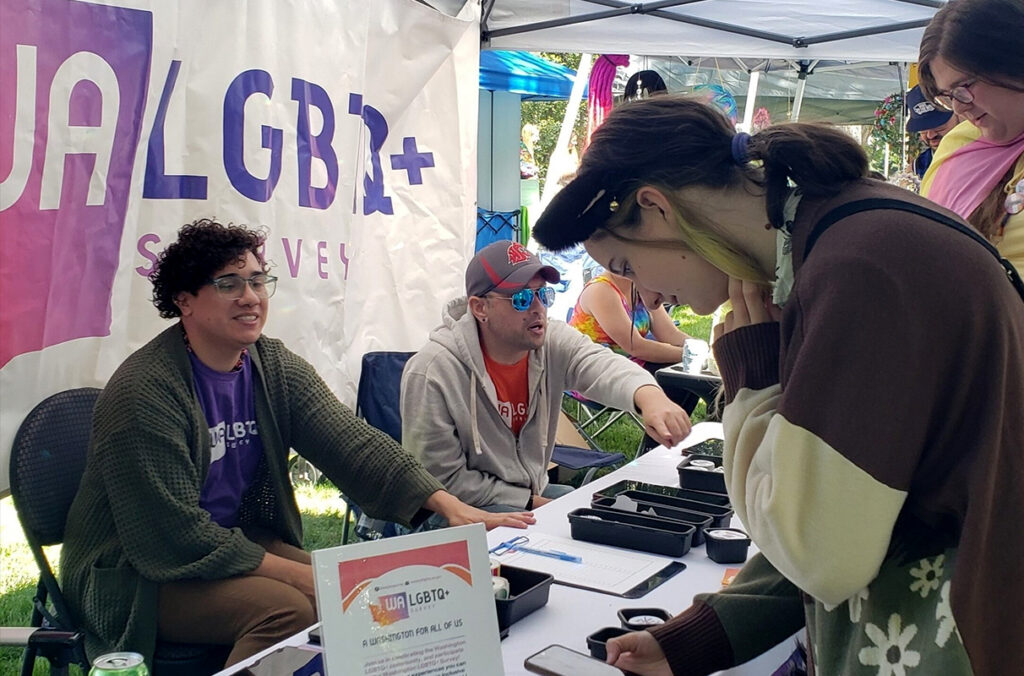 LGBTQ+ people taking a survey at a community festival booth.