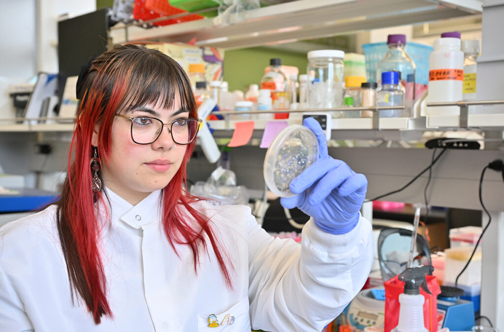 Anastasia Martinez holding and examining a Petri dish in a research lab.
