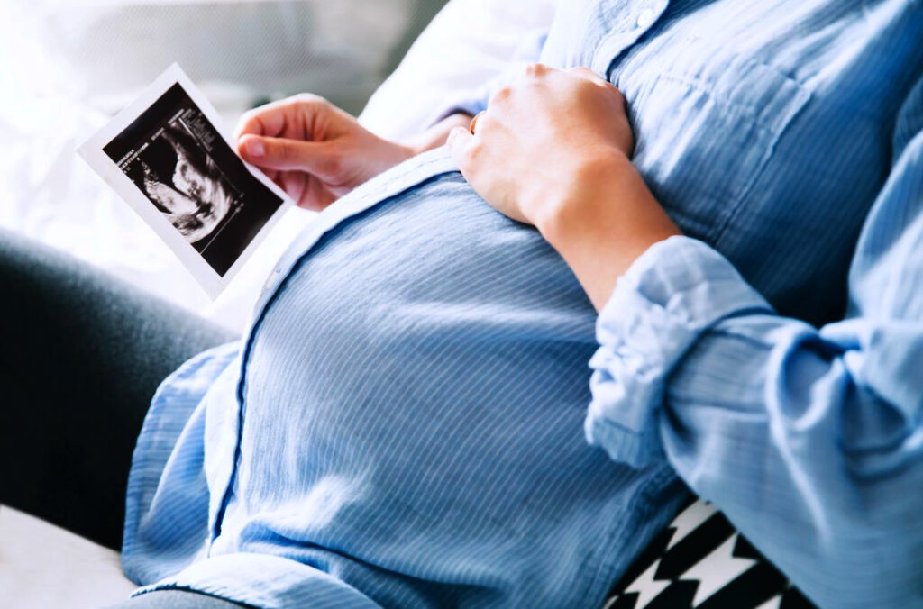 A pregnant mother holds a hand on her belly while looking at a printed ultrasound image.