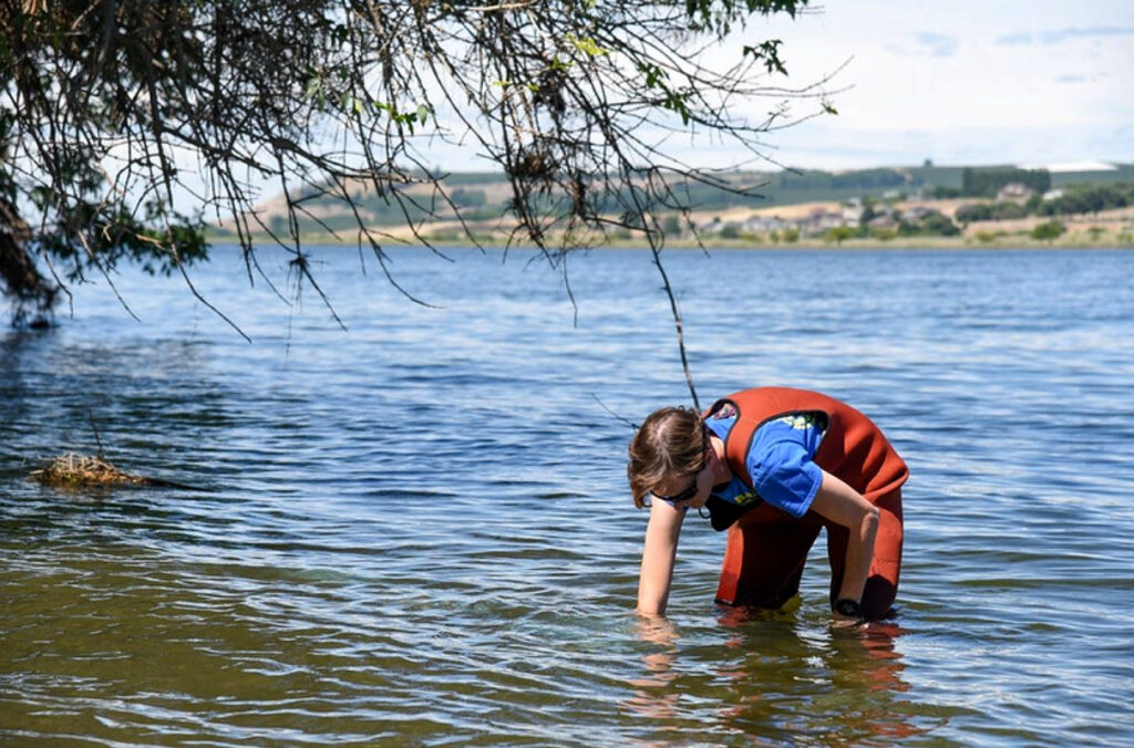 Sarah Roley standing in knee-deep water near the bank of the Yakima River.