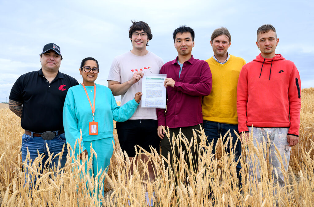 Six researchers standing in a wheat field holding the first page of their published journal article.