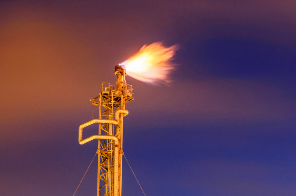An industrial chimney tower flares gas against a dark sky.