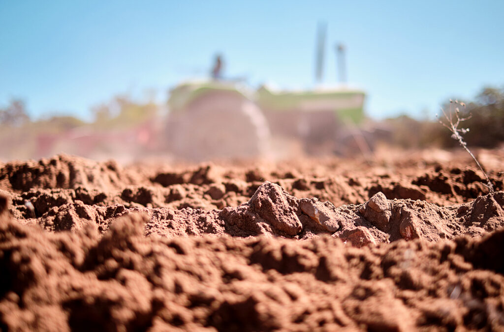 Closeup of a dirt field as a tractor plows in the distance.
