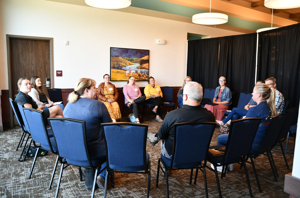 People seated in chairs in a circle inside a conference room at a youth mental health summit.