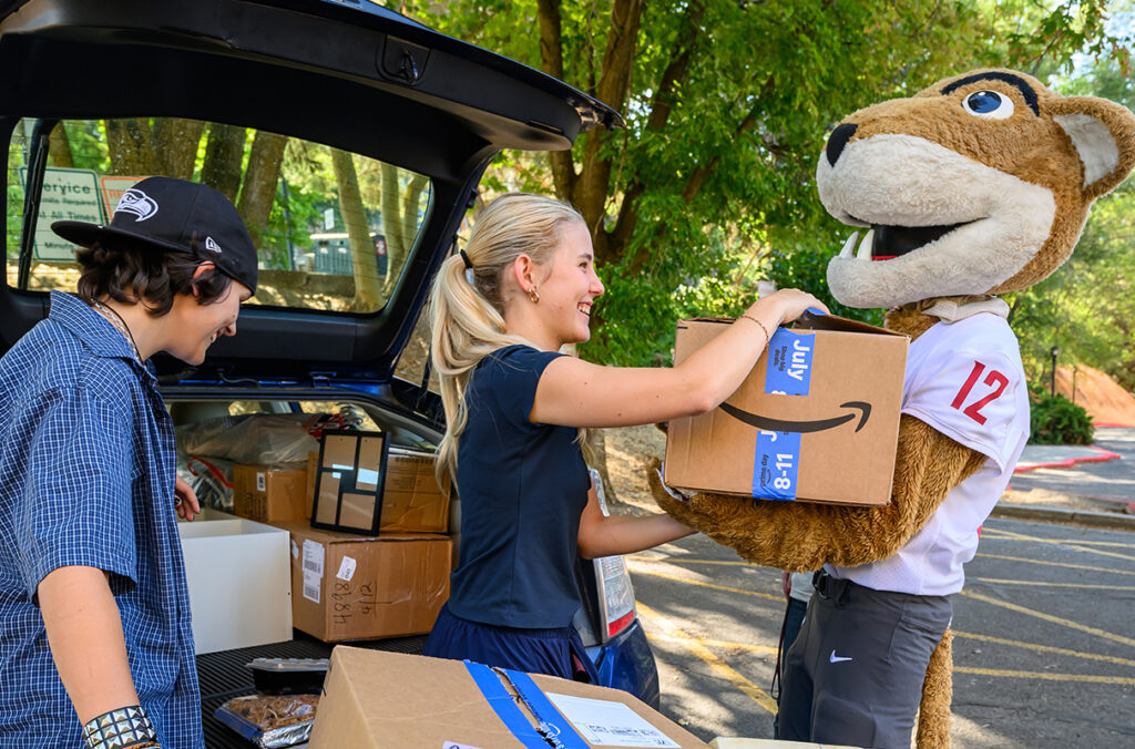 One of two students unloading a car handing Butch a box to carry.